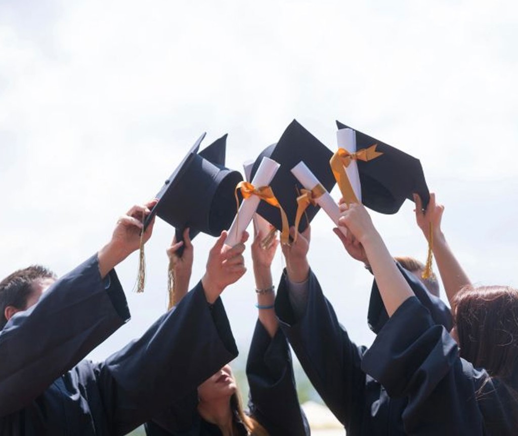 Students holding graduation caps and diplomas in celebration